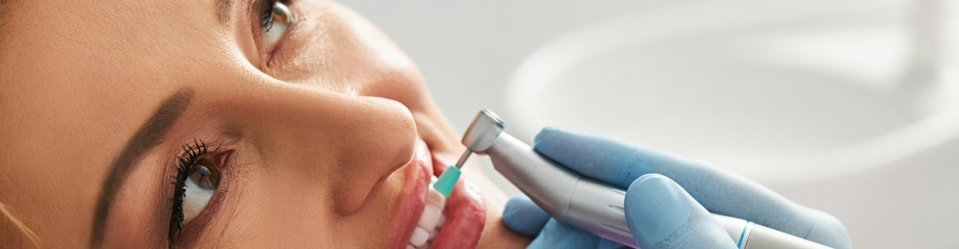 Gloved hand using dental tool in woman's mouth.